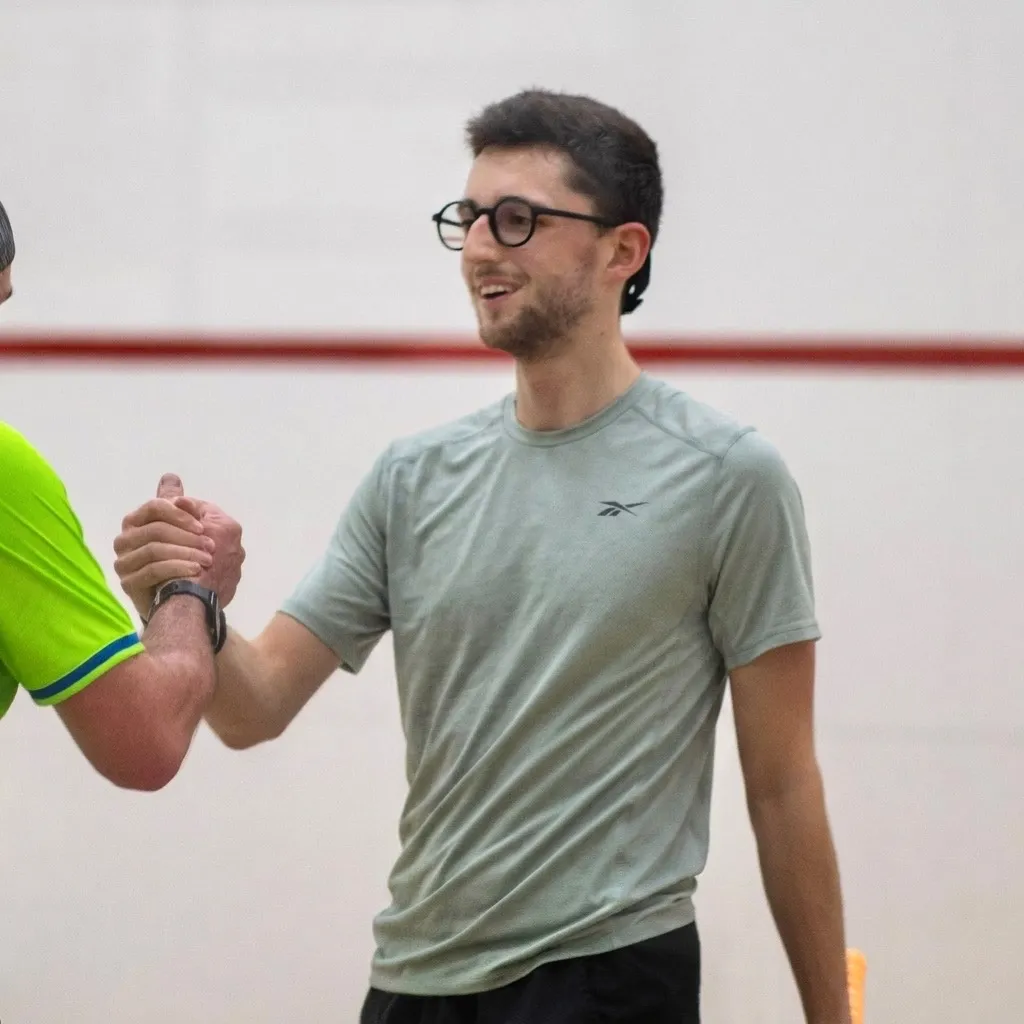 Alex Demars, souriant, serre la main d’un joueur sur un terrain de squash.